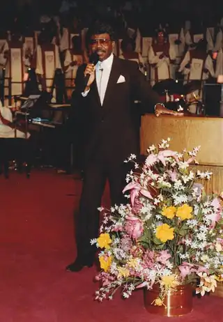 Pastor Clinton Utterbach holding a microphone during a church service, from the family archive.
