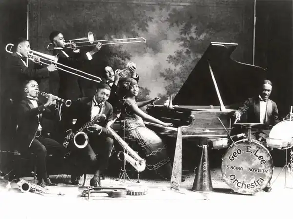 Archival George E. Lee Singing Novelty Orchestra photograph, with musicians gathered around a piano and drums.